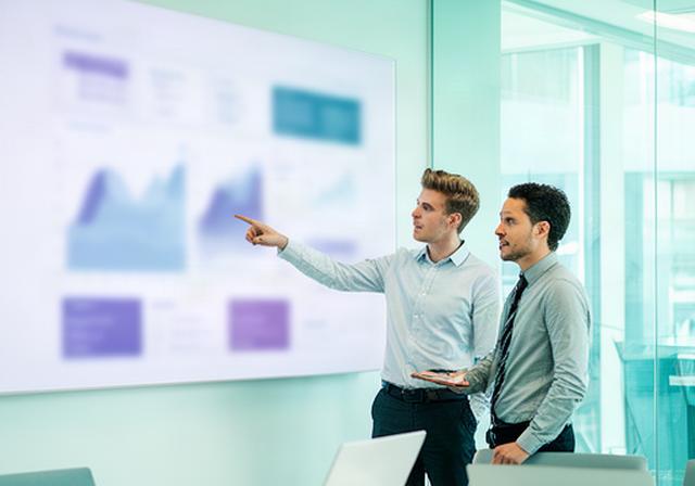 Operations analysts reviewing performance charts on a large screen in a bright Milton Keynes office