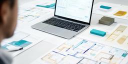 Retail analyst comparing customer demand charts on a laptop beside printed store plans